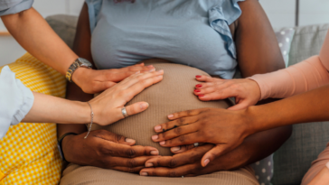 A group of people resting their hands on a pregnant woman's stomach.