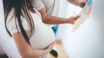 A pregnant woman holding her tummy and looking at paint samples.