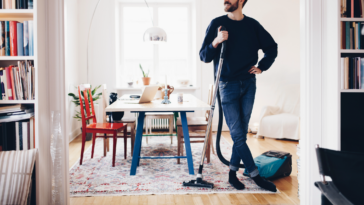 A man leaning on a vacuum in the living room