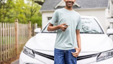 Portrait of a teenage boy holding keys in front of his first car.