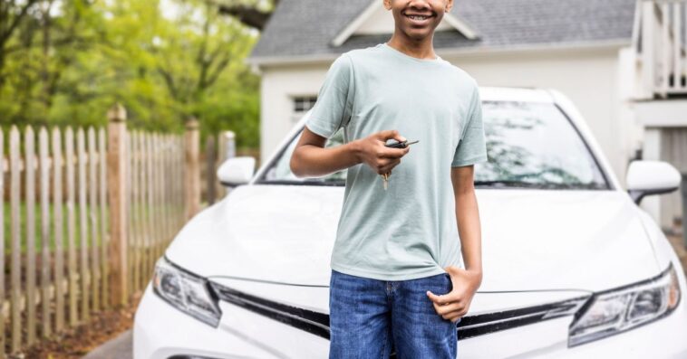 Portrait of a teenage boy holding keys in front of his first car.