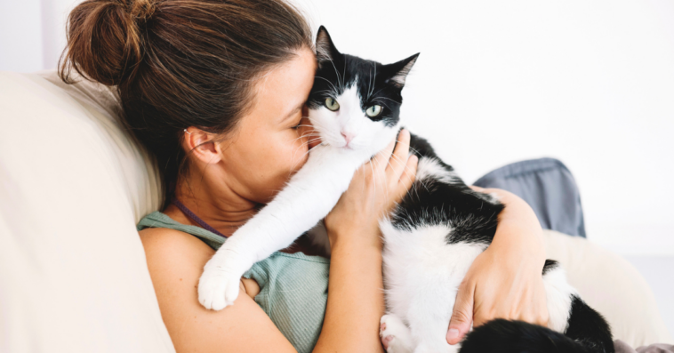 A woman snuggling up with a black and white cat on the sofa.