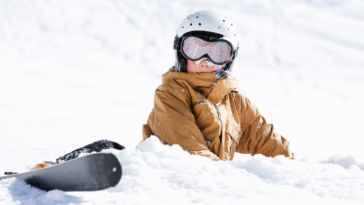 A boy lying down in the snow wearing ski gear.