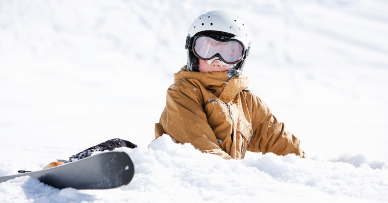 A boy lying down in the snow wearing ski gear.