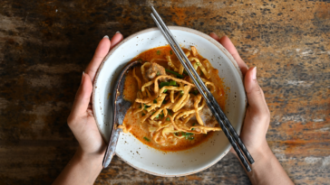 hands holding bowl of Khao Soi Thai food with spoon and chopsticks