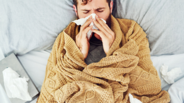 man wrapped in blanket blows nose