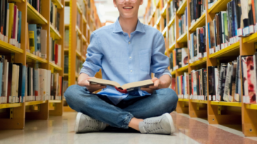 teen boy sitting on library floor looking at a book