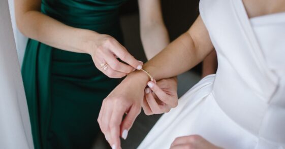 Bridesmaid in green gown helps a gorgeous bride to dress up and get ready for her wedding ceremony.