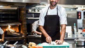 Portrait of male chef preparing food at a counter. He is working in commercial kitchen.