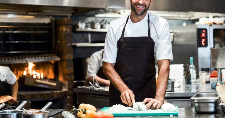 Portrait of male chef preparing food at a counter. He is working in commercial kitchen.