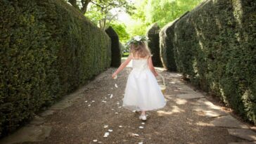 Shot from behind of a flower girl sprinkling petals in a garden.