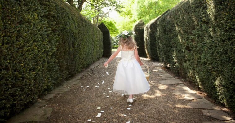 Shot from behind of a flower girl sprinkling petals in a garden.