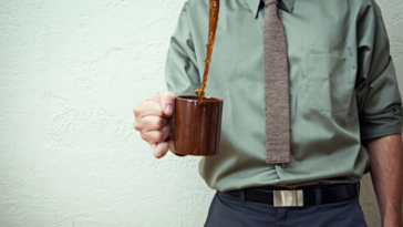 A man holding a cup of coffee with coffee spilling out of it.