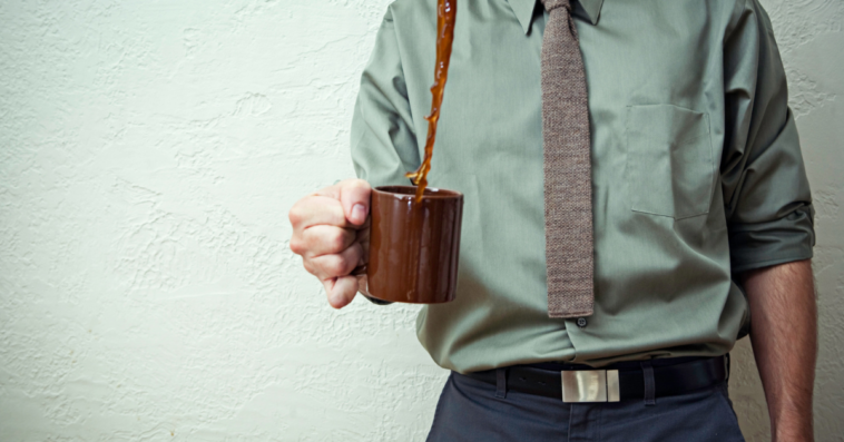 A man holding a cup of coffee with coffee spilling out of it.