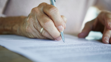 An elderly woman signing a piece of paper.