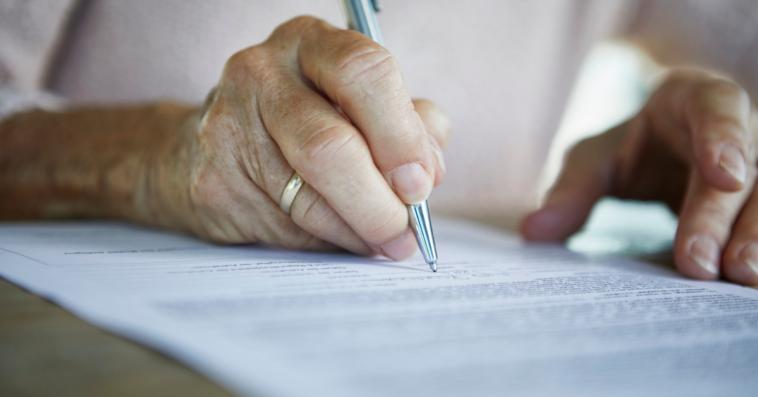 An elderly woman signing a piece of paper.