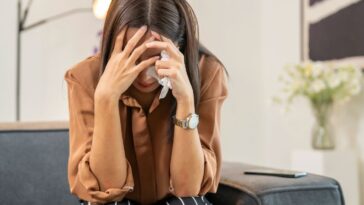 A stressed out young woman covering her face with hands and crying.