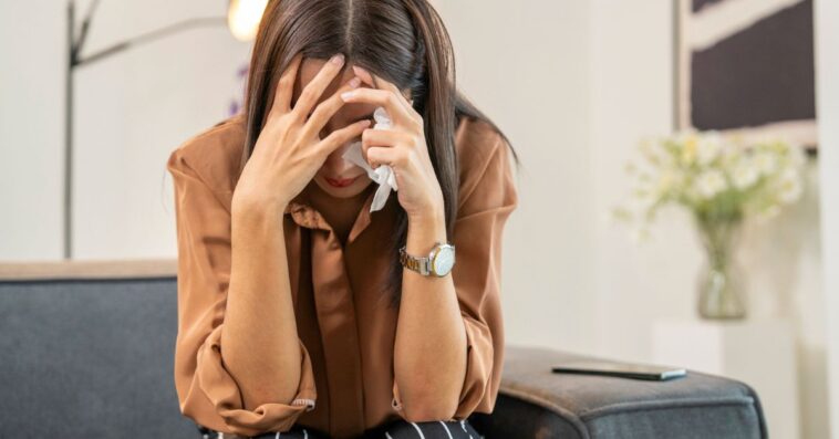 A stressed out young woman covering her face with hands and crying.