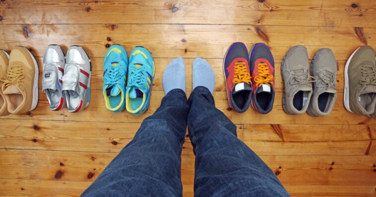 A shot of a person's feet surrounded by shoes on a wooden floor.