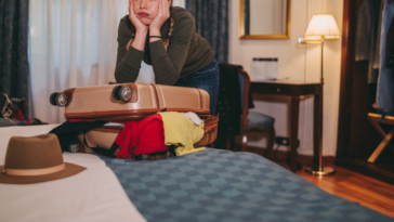 A teenage girl leaning on a stuffed suitcase on a bed.