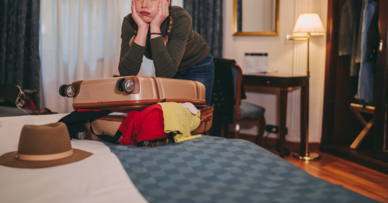 A teenage girl leaning on a stuffed suitcase on a bed.