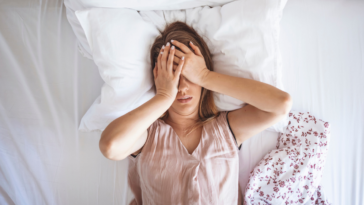 A woman lying in bed with her hands over her eyes.