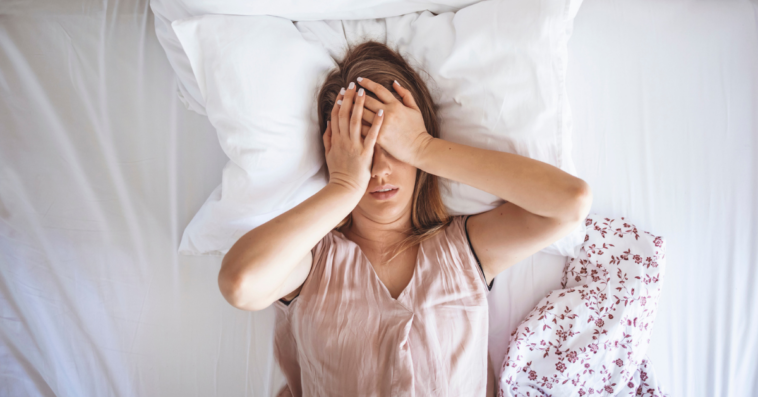 A woman lying in bed with her hands over her eyes.