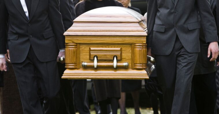People carry a casket at an outdoor cemetary.