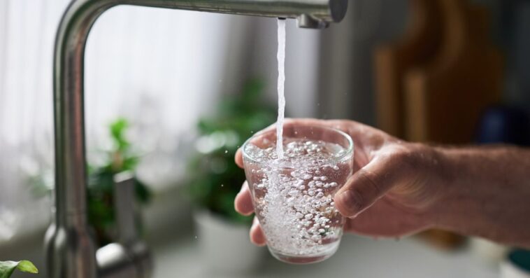 Person filling glass of water from kitchen sink