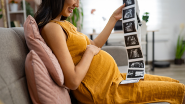 A pregnant woman resting her hand on her belly and holding sonogram pictures.