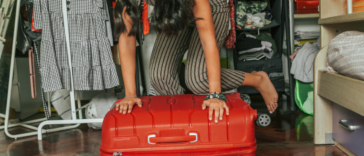 A woman kneeling on top of a suitcase.