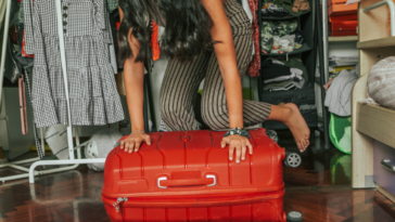 A woman kneeling on top of a suitcase.