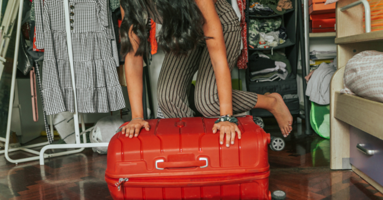 A woman kneeling on top of a suitcase.