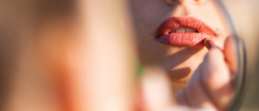 A woman applying red lipstick to her lips.