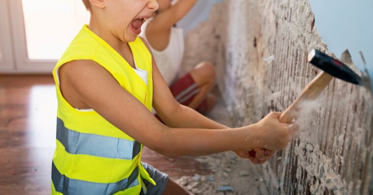 Two little manual workers renovating their room. Boys aged 7 are tearing out plaster from the walls using hammer and chisel.