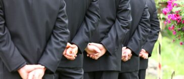 A lineup of groomsmen hands clasped during the wedding ceremony.