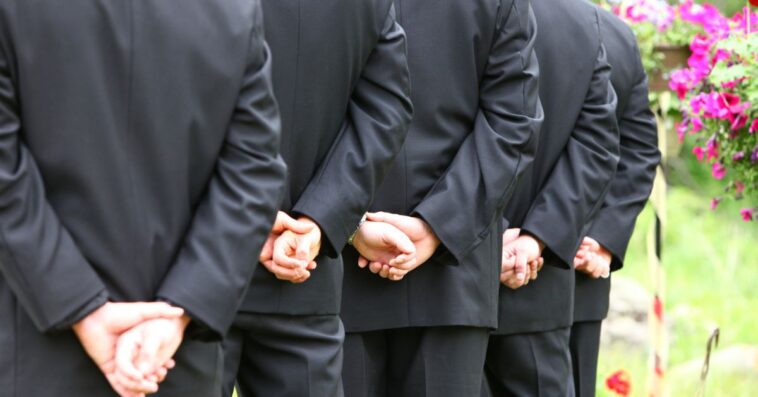 A lineup of groomsmen hands clasped during the wedding ceremony.