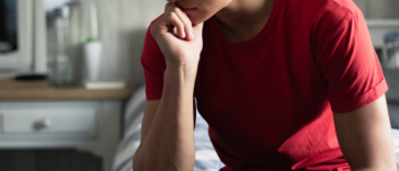 A pensive teen boy in a red shirt with hand on his chin.