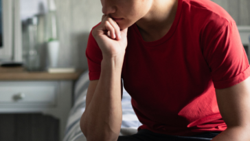 A pensive teen boy in a red shirt with hand on his chin.