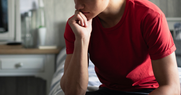 A pensive teen boy in a red shirt with hand on his chin.