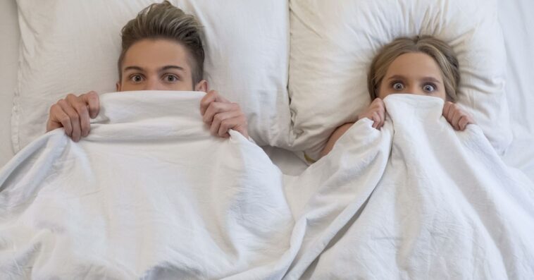 Lovers caught in bed by parents, embarrassed and frightened, looking shocked.