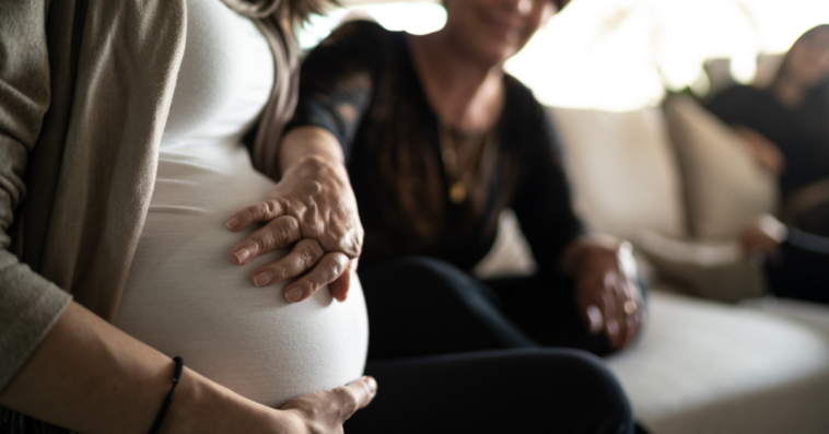 A woman touching a pregnant woman's belly.