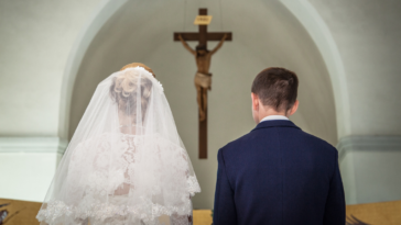 bride and groom kneeling in church before a rood