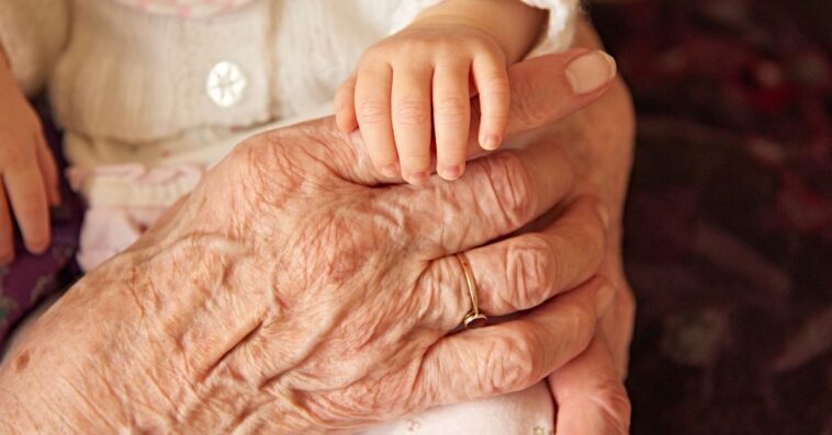 Infant holding an elderly person's hand