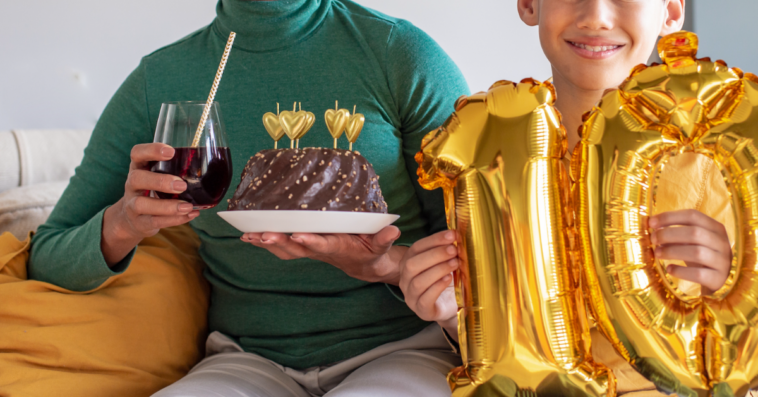 A you holding golden number 10 balloons sitting next to a woman holding a cake and a drink.