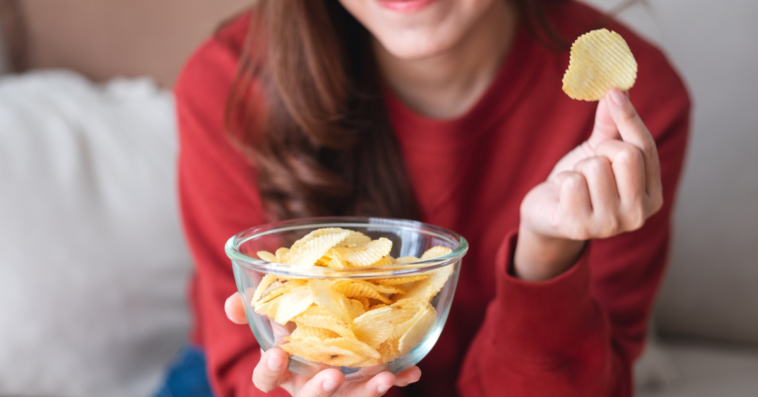 A woman holding a bowl of potato chips in one hand and a single potato chip in another.