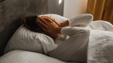 woman laying in bed with hands covering face