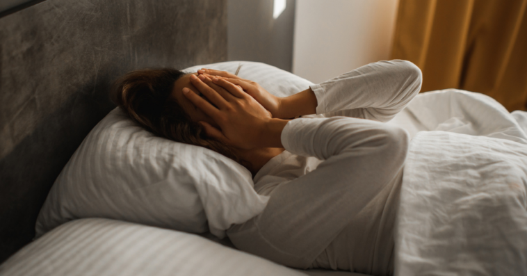 woman laying in bed with hands covering face