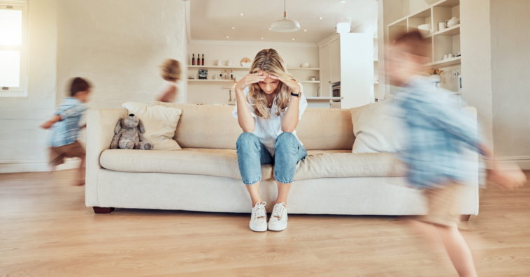 woman seatedon couch with headin hands as kids run around