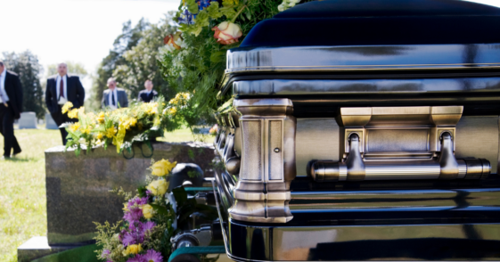men in suits in cemetery with casket in foreground